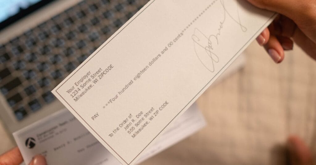 Individual holding a cheque over laptop, signifying online banking or financial transaction.